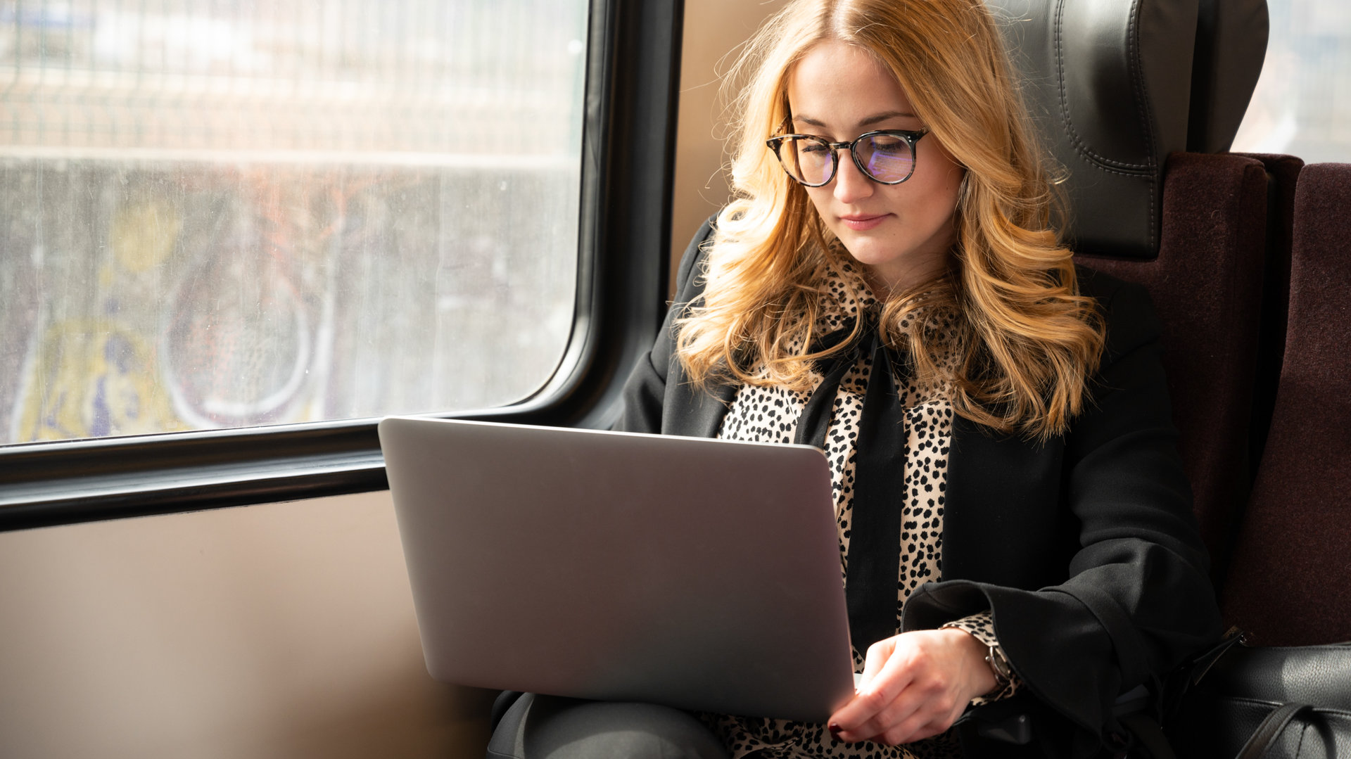 A girl with glasses working on her laptop on the train